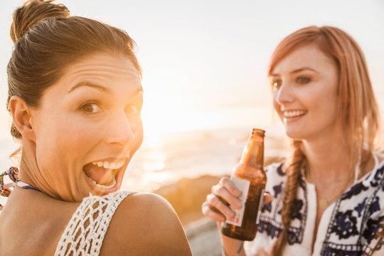 Portrait of two mid adult female friends pulling faces on beach at sunset, Cape Town, South Africa