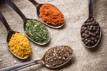 Spices on old metal spoons. Linen fabric background.