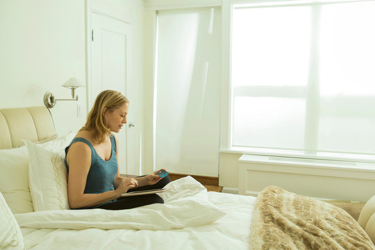 Woman sitting on bed reading update on digital tablet