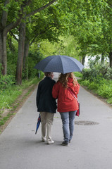 Frauen mit Regenschirm gehen einen Weg entlang / Aufnahme zeigt zwei Frauen, unterschiedlichen...