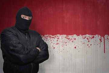 dangerous man in a mask standing near a wall with painted national flag of indonesia