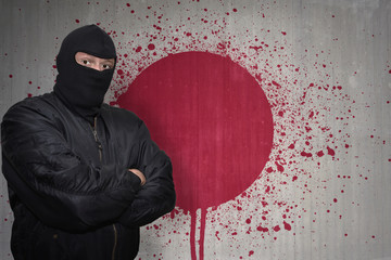 dangerous man in a mask standing near a wall with painted national flag of japan