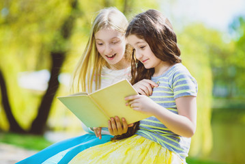 Children reading books at park. Girls sitting against trees and lake outdoor