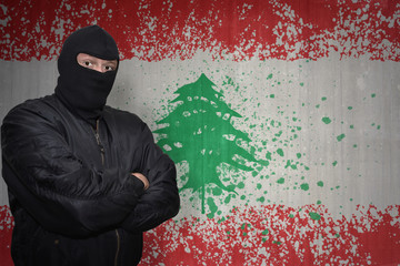 dangerous man in a mask standing near a wall with painted national flag of lebanon