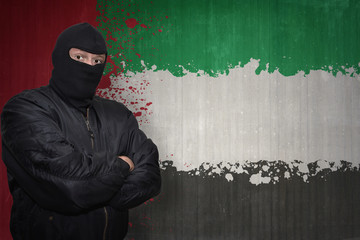 dangerous man in a mask standing near a wall with painted national flag of united arab emirates