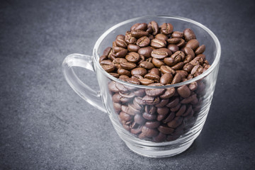 Coffee seeds in transparent cup on black surface background.