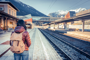 Girl waiting train on the platform, in the background snow-capped mountains. Traveling by train at the Alpine Railroad