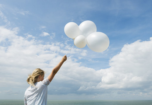 Girl holding white balloons outdoors
