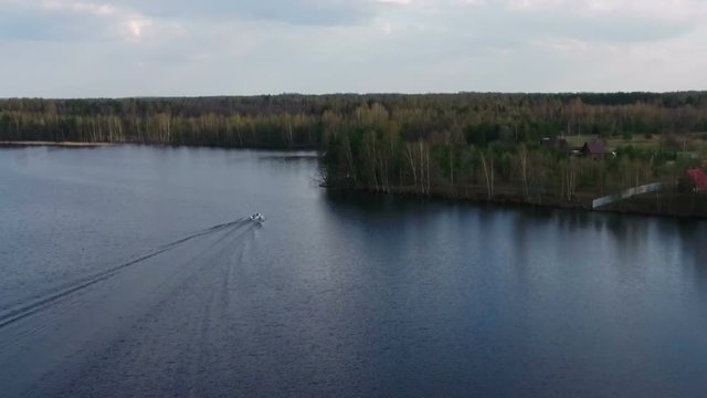 Camera flying over big lake to the shore with riding speed boat on water, Russia
