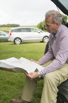 Man sitting on car boot reading map