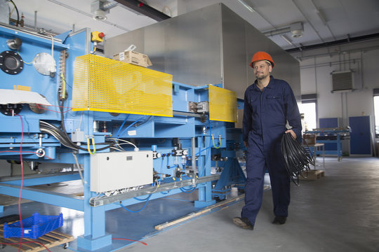 Worker carrying reel of cable in industrial plant