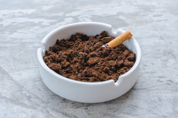 Cigarette and coffee ground on the ceramic ashtray.
