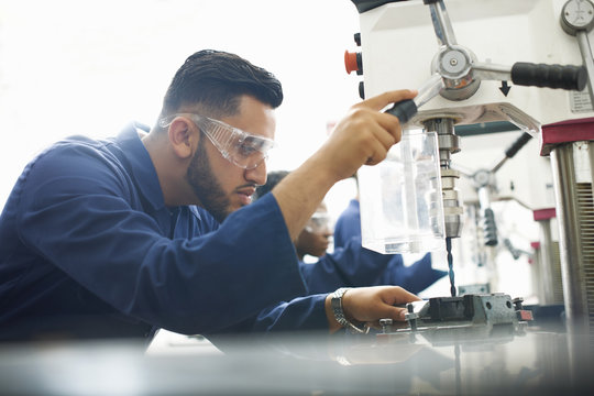Male student using drilling machine in college workshop