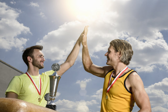 Two male gymnasts with trophies giving each other high five