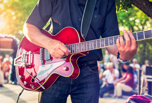Man with a red electric guitar in the park playing a summer concert
