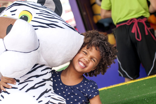 Portrait of girl in front of amusement stall carrying large prize tiger toy