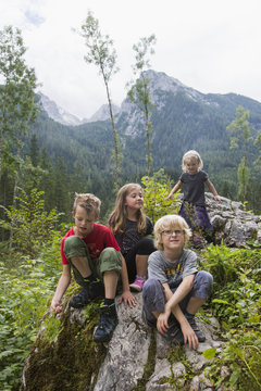 Brothers and sisters sitting on rock formation in forest, Zauberwald, Bavaria, Germany