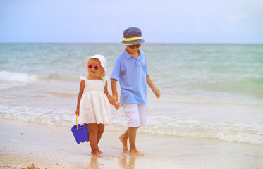 cute little boy and toddler girl walk on beach