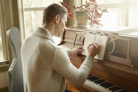 Young man writing in notebook whilst at the piano
