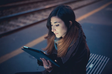 Mid adult woman using digital tablet on railway platform at dusk