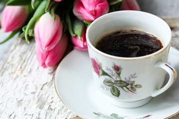 Cup of coffe in a floral cup with tulip flowers in background