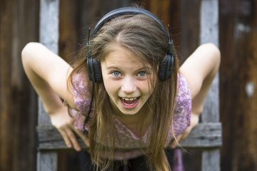 Emotional naughty little girl with headphones, close-up portrait outdoors.