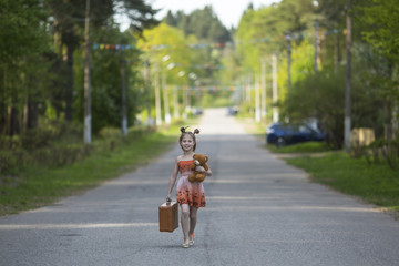 Little girl with suitcase walking along the road.