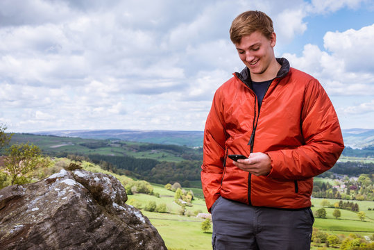 Male teenage hiker reading smartphone texts on top of Guise Cliff, Pateley Bridge, Nidderdale, Yorkshire Dales