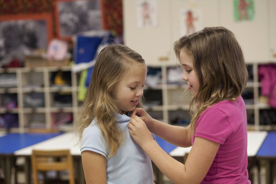 Girl buttoning friend's tee shirt in classroom