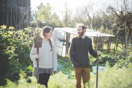 Young Couple In Garden Holding Fork And Spade