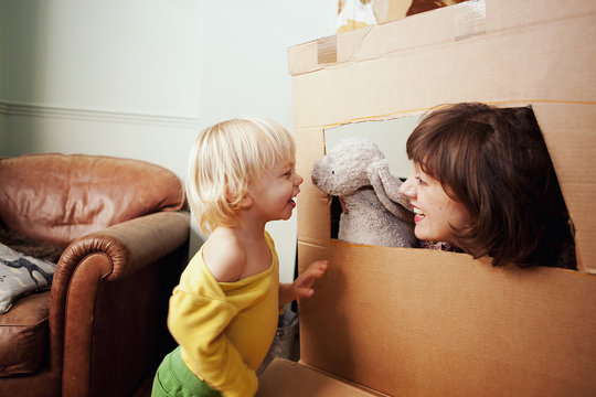 Mother and son playing with cardboard box window in living room
