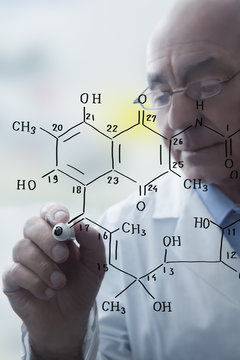 Senior male scientist writing molecular formula on clear board