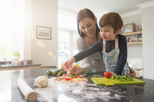 Mother and son preparing pizza together in kitchen