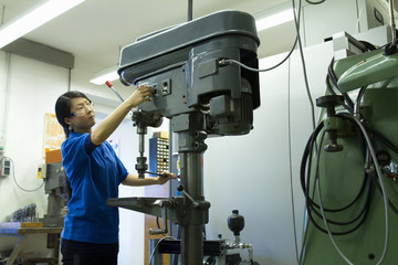 Young woman adjusting drill in industrial workshop