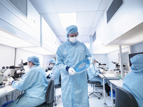 Electronics worker in clean room holding silicon wafer