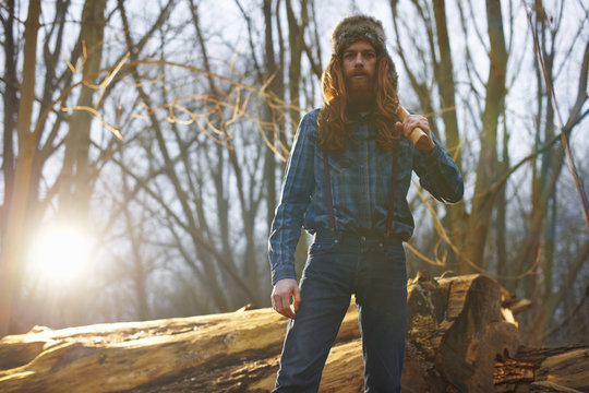 Man in trapper hat chopping wood in countryside