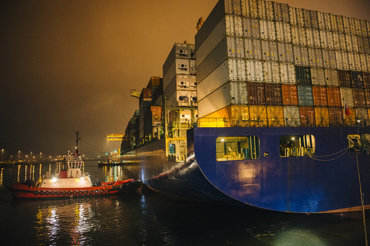 Tugboat manoeuvring container ship on river at night, Tacoma, Washington, USA