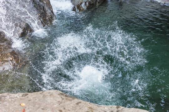 A splash from someone jumping into a swimming hole in the woods with a waterfall