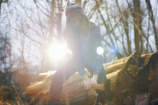 Man in trapper hat chopping wood in countryside