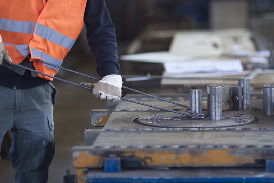 Factory worker bending metal rod in concrete reinforcement factory
