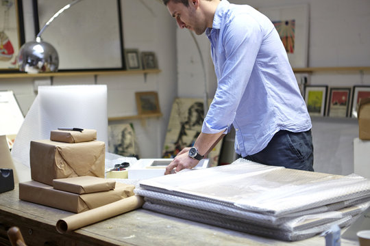 Man wrapping frames in bubble wrap on table in picture framers workshop