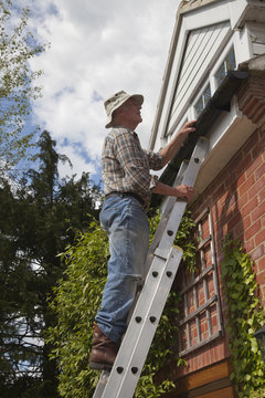 Senior man on ladder fixing gutter