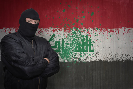 dangerous man in a mask standing near a wall with painted national flag of iraq