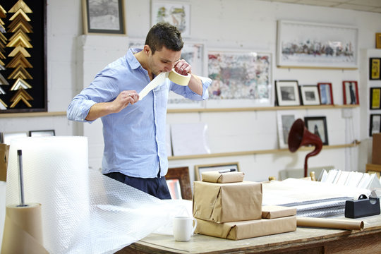 Man bubble wrapping frame on table in picture framers workshop