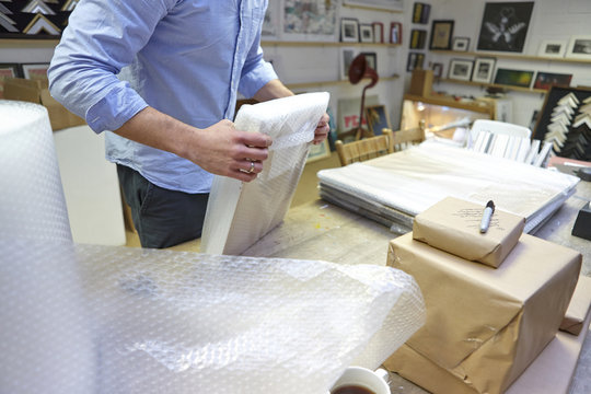 Man bubble wrapping picture frame on table in picture framers workshop