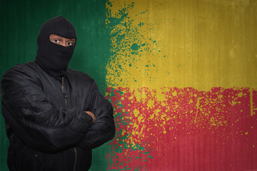 dangerous man in a mask standing near a wall with painted national flag of benin