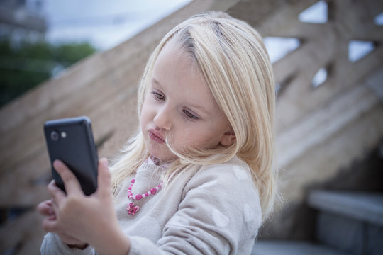 Confused young girl on stairway using smartphone, Cagliari, Sardinia, Italy