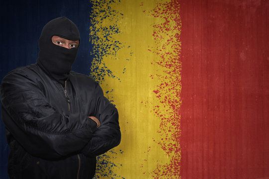dangerous man in a mask standing near a wall with painted national flag of chad