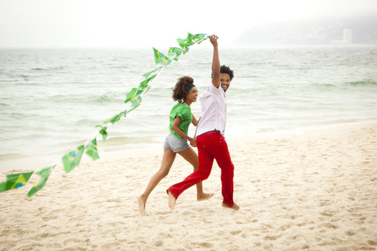 Couple playing with string of flags on beach, Rio de Janeiro, Brazil