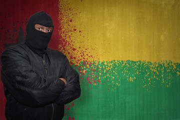 dangerous man in a mask standing near a wall with painted national flag of guinea bissau
